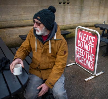 A man sits on a picnic bench holding a mug of tea.