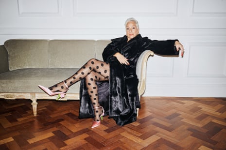 Denise Welch wearing a long, black faux-fur coat, sheer tights with black polka dots on and pale-pink, high-heeled shoes