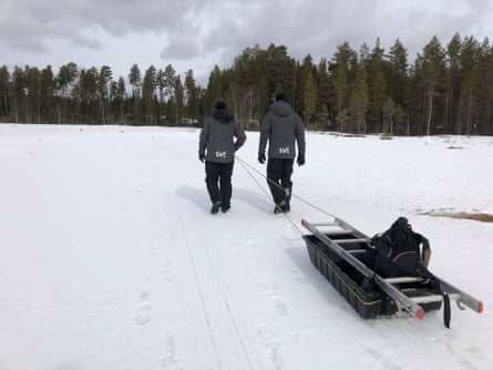 Two people walking in the snow carrying a sledge with a ladder and material in it