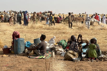 An African family sit surrounded by their meagre possessions with a crowd of other displaced people and the occasional donkey and cart in the background