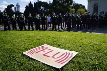 A sign reading ‘FLU’ sits on the grass in front of police and protesters