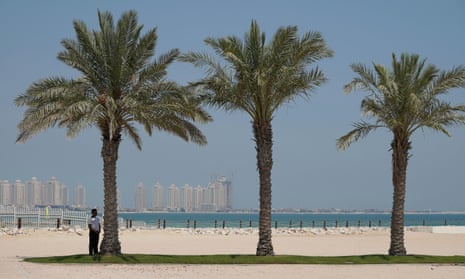 A security guard stands in the shade of a palm on a hotel beach in the Gulf