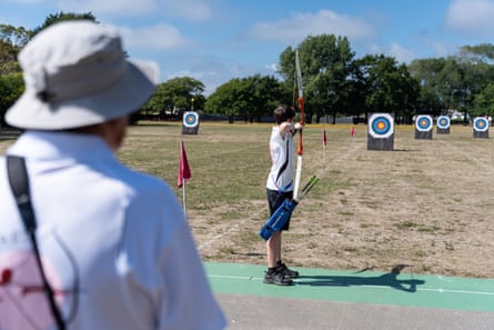 A young archer takes aim while someone watches