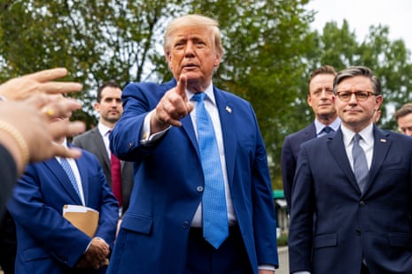 Man in a blue suit points forward as people hold their hands out to get his attention