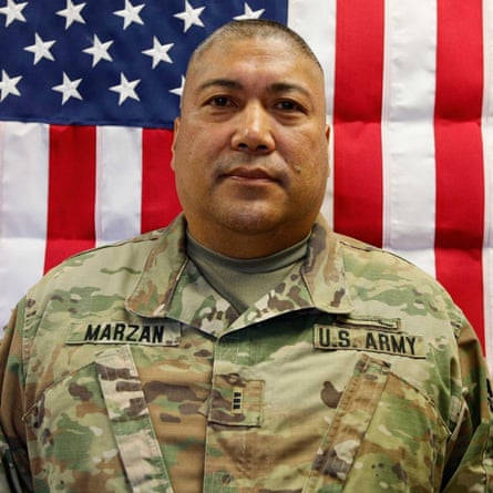 a man in a soldier’s uniform stands in front of a US flag