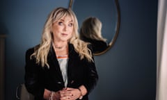 Helen Lederer in a black jacket stands with her back to a mirror.