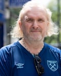 Jim Munro, with a beard, longish hair and his sunglasses hooked onto the collar of his sports shirt saying “Umbro” and “West Ham”, squints into the sun