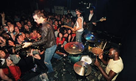 Musicians onstage in a tiny, packed venue seen from a high angle backstage