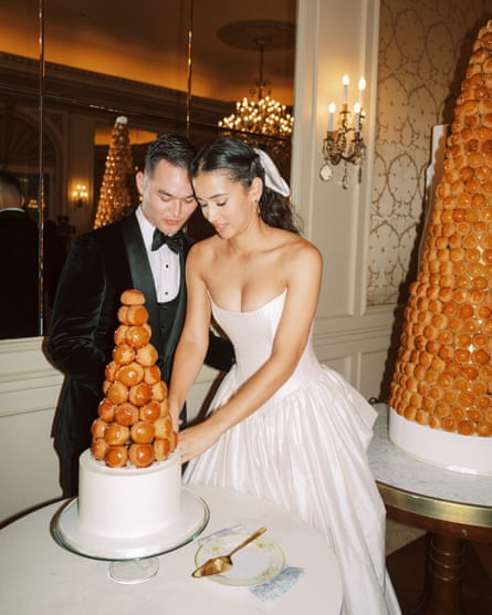 a bride and groom cutting a croquembouche cake. her dress is strapless with a drop waist