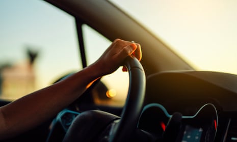 Female hand holding steering wheel in a car during a drive at sunset