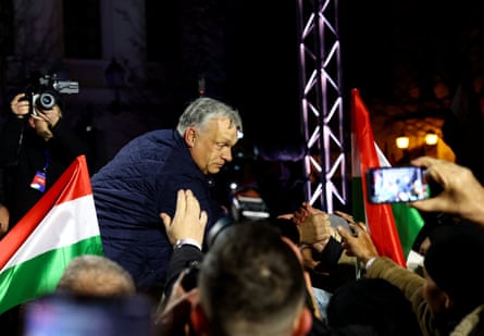 Viktor Orbán reaches down from a stage to shake hands with supporters in a crowd holding Hungarian flags