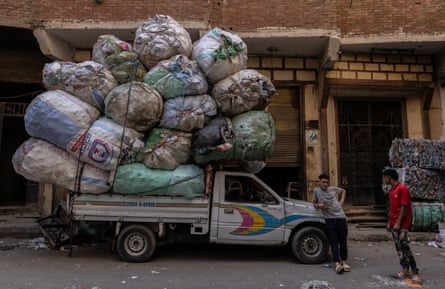 Two men stand next to a pickup truck piled high with bags of rubbish