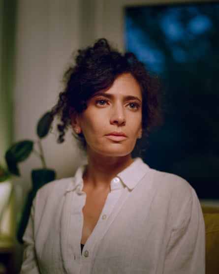 A woman with dark curly hair wears a white button down shirt and poses for a photo inside a home