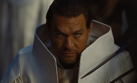 Momoa in white suit with massive rigid collar faces forward while eyes look upward
