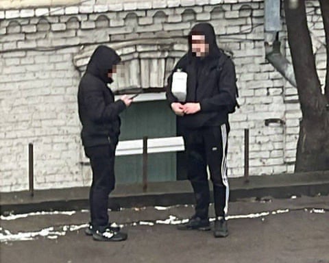 Two young men, one on his phone and the other carrying a box
