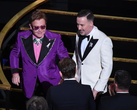 Elton John and David Furnish in similar purple and white outfits.