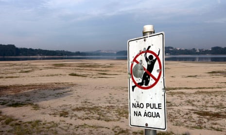 A bullet-ridden sign warning people not to jump into the water in the dried-up Guarapiranga reservoir.