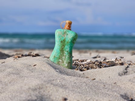 A colourful plastic bottle stands in the sand on a beach.