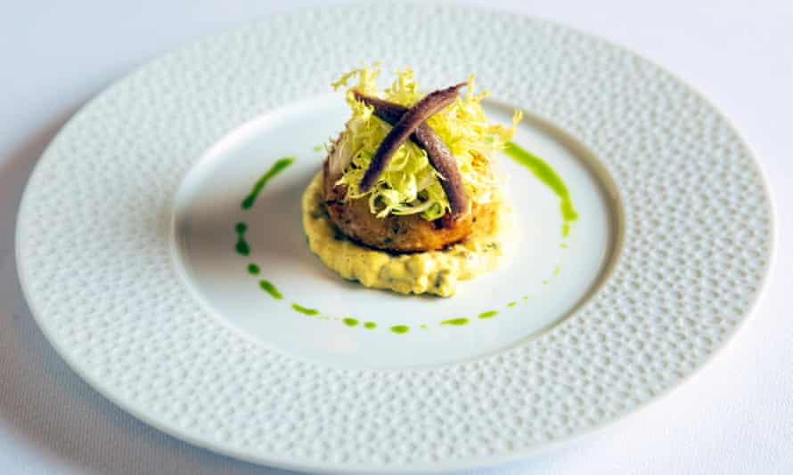 Smoked haddock fishcake with a ring of green oil around it and two crisscrossed anchovies on top
