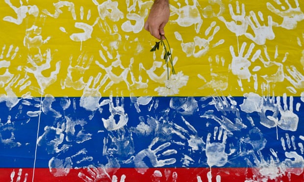A man places a flower on a Colombian national flag during a march along the streets of Cali, Colombia, in 2016, in support of peace talks. Despite a historic peace deal, bloodshed continues.