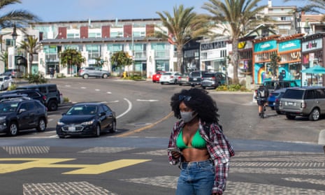 A woman wearing a face mask crosses the street in Hermosa Beach on Tuesday, the day after Governor Gavin Newsom rolled back California’s reopening.