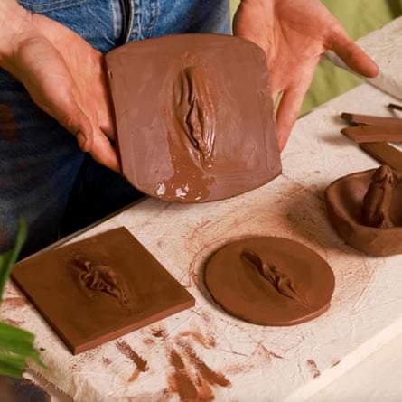 Someone holds a clay tile with an imprint of a vulva
