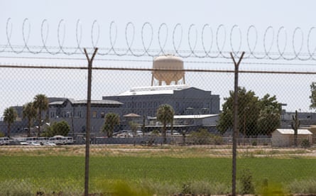 A prison surrounded by a wide grassy lawn and a chain-link fence topped by razor wire.