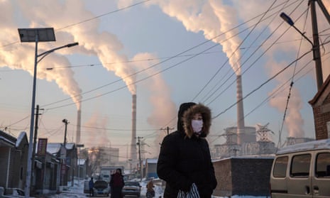 Smoke billows from stacks as a Chinese woman wears as mask while walking in a neighbourhood next to a coal fired power plant