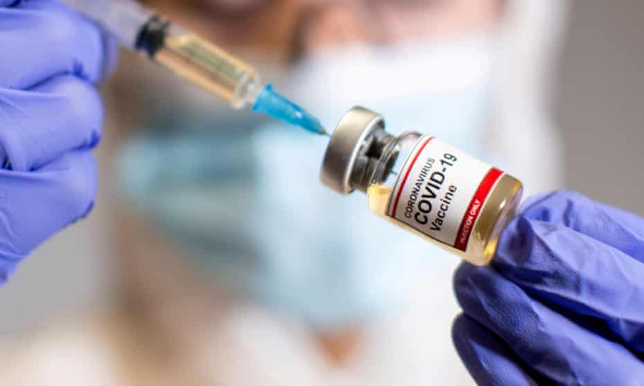 A woman holds a medical syringe and a small bottle labeled “Coronavirus COVID-19 vaccine”.