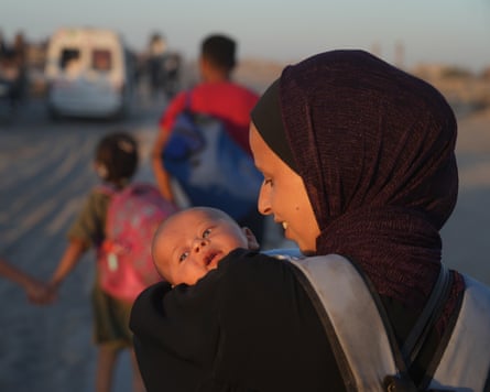 A Palestinian woman carries her baby as she walks with others heading toward Gaza City