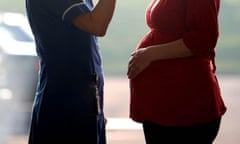 A pregnant woman and a midwife, seen from the shoulders down, stand facing each other