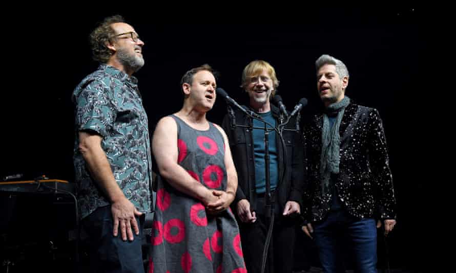 Phish's four members sing around a microphone