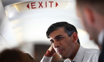 Rishi Sunak looking pensive under an airplane exit sign