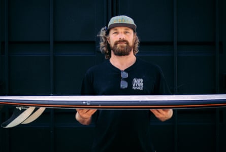 A man in O’Neill baseball cap and t-shirt holds a surfboard
