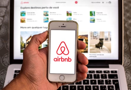 The Airbnb logo on a smartphone in front of a laptop showing its website