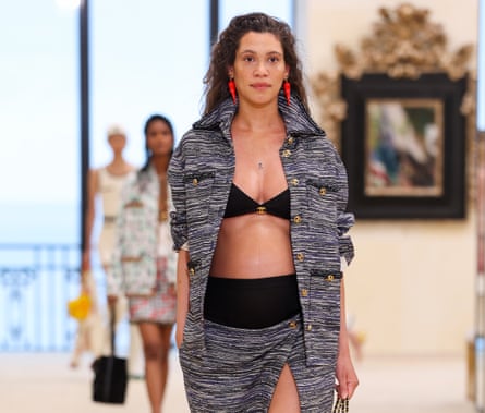 A pregnant model wearing a black bikini with a black and white toned suit jacket and skirt over the top