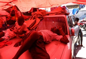A man and a boy rest on a car bonnet under a tarpaulin
