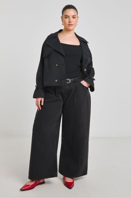 A model wearing a black cropped trench coat and black denim jeans