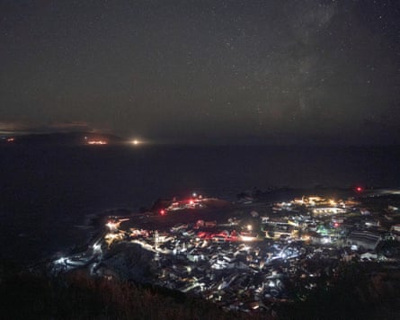 Aerial view of a village glowing with white and red lights at night under a star-filled sky