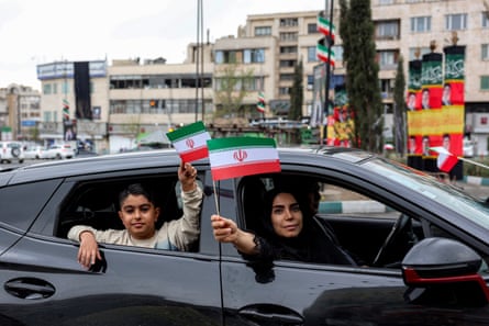 A woman and boy hold up miniature Iranian flags while sitting in a vehicle