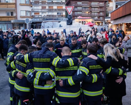A ring of Swiss firefighters with their arms around each other and their heads bowed