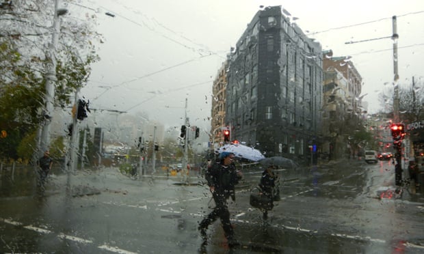 Pedestrians holding umbrellas cross a Sydney street in the rain