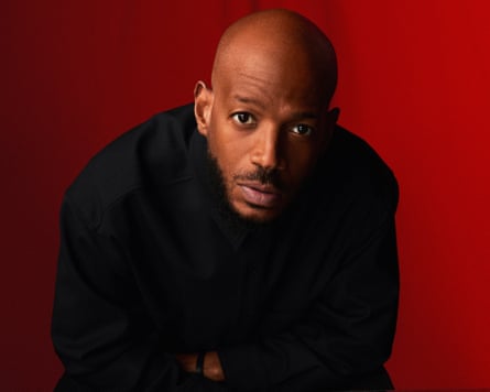 A photograph of Marlon Wayans looking at the camera, in front of a dark red background.