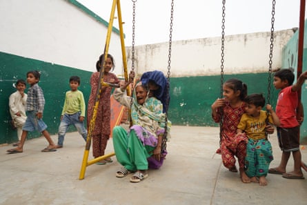 أما، 92 عامًا، تجلس على أرجوحة وسط الأطفال في ساحة المدرسة.