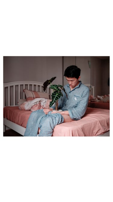 A man sitting on a bed in pyjamas with a plant pot between his legs