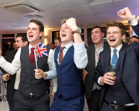 Young men dressed in suits and holding union flags cheer and raise their fists in triumph.