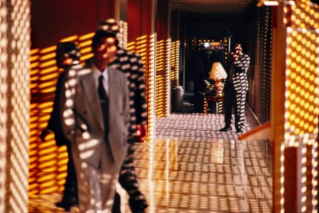 Two men standing and two others walking in a hotel lobby with yellow walls patterned by the shadows of blinds and screens
