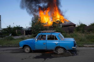 A Ukrainian man drives his car past a burning house hit by a shell on the outskirts of Bakhmut
