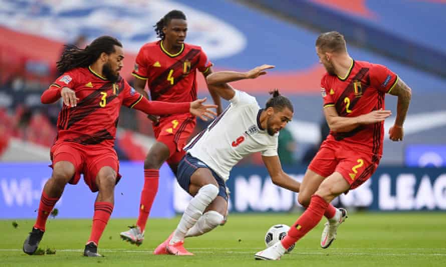 Un joueur anglais en chemise blanche avec le ballon tente de traverser un groupe de trois défenseurs en rouge qui l'entoure
