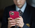A young person in school uniform holds a red-cased iPhone with both hands